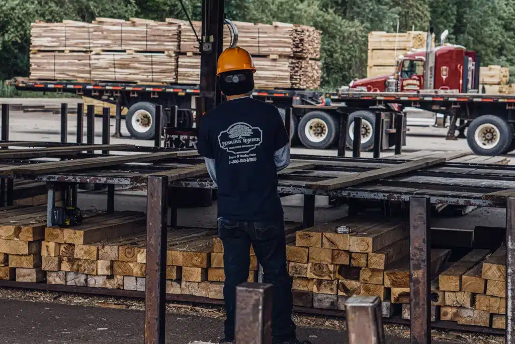 Buskirk Lumber employee assembles cut lumber in a sawmill facility. Outside, two semi trucks are loaded with cut lumber.