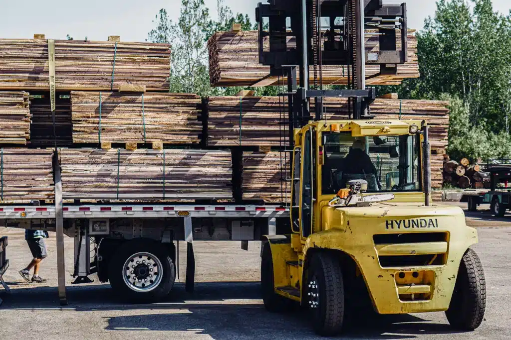 Buskirk Lumber employee uses a yellow Hyundai forklift to stack bundles of cut lumber onto the trailer of a semi truck.