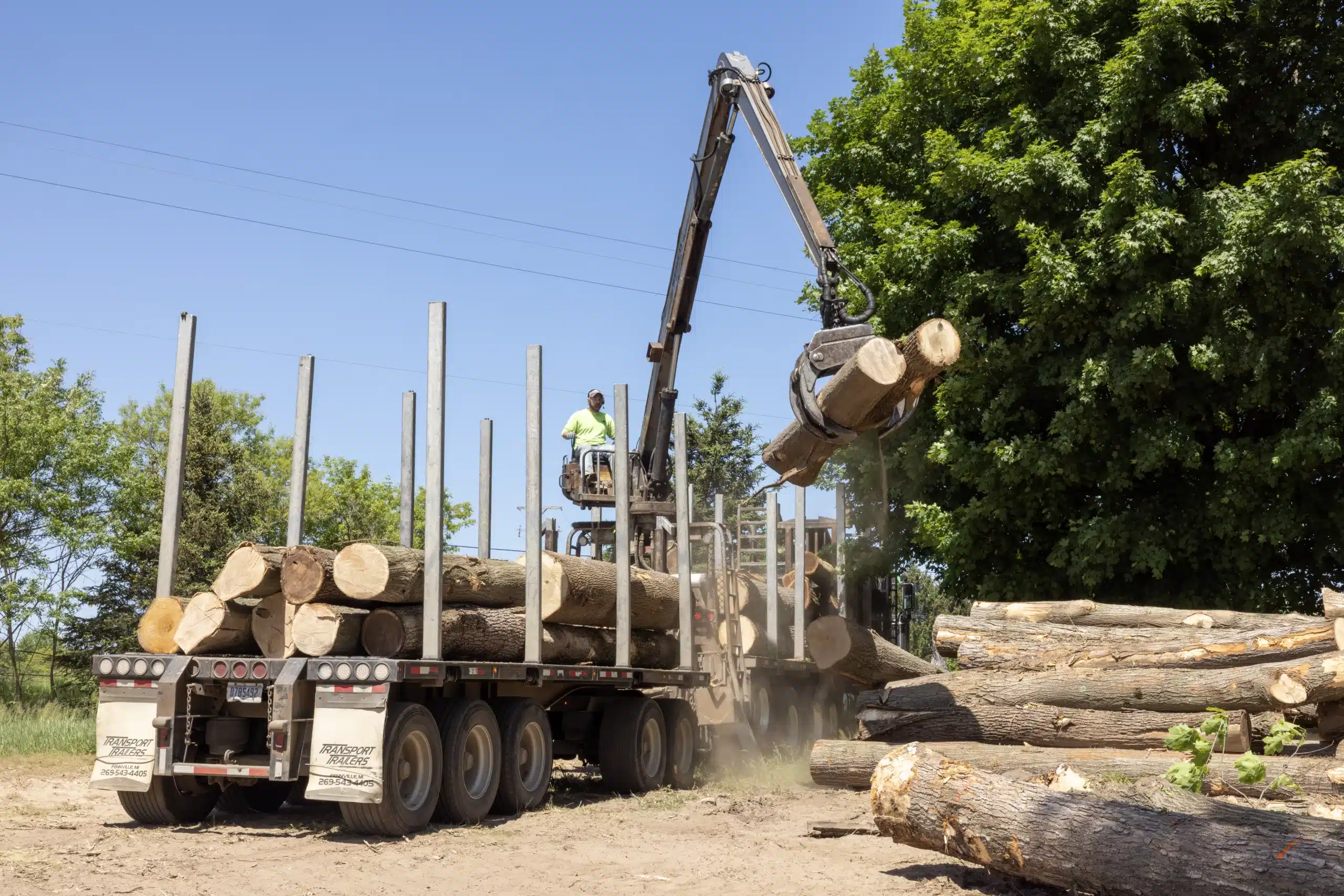 A Buskirk Lumber employee-operated log loader truck lifts two timber logs onto its flatbed trailer.