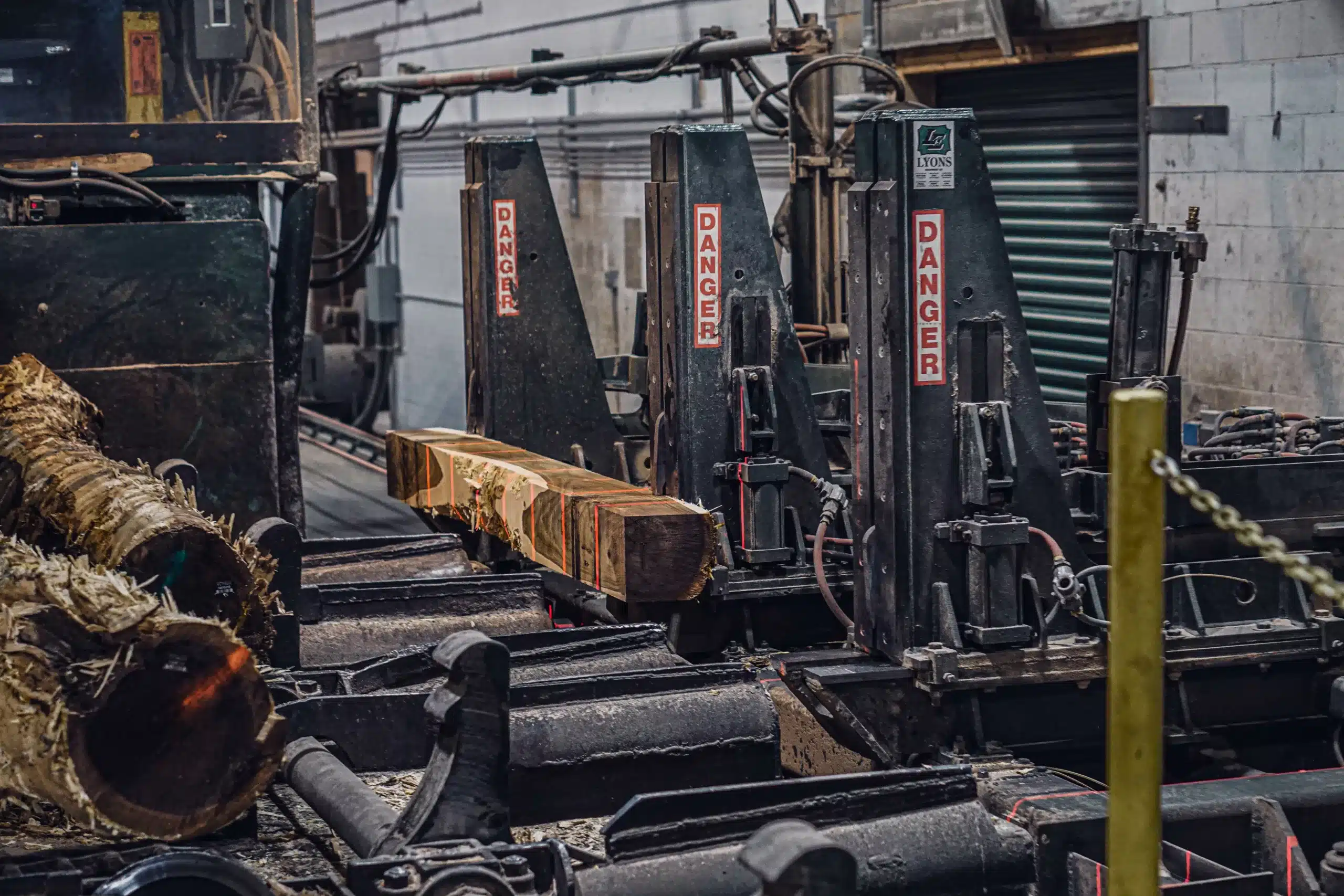 A timber log passes along a conveyor belt to a Filer & Stowell Co. band head saw, which takes off the edges of the logs.